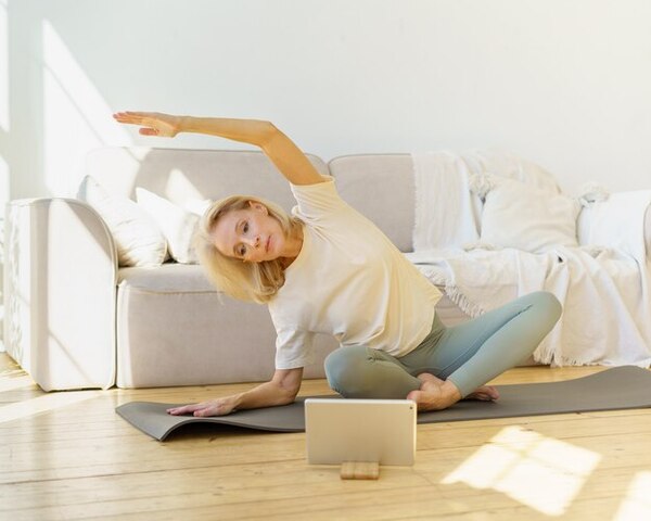 Pessoa adulta sentada num tapete a alongar suavemente o corpo em casa